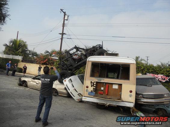 person photographs a chaotic scene of multiple wrecked vehicles, including a bus and a buggy, piled on top of each other on a street