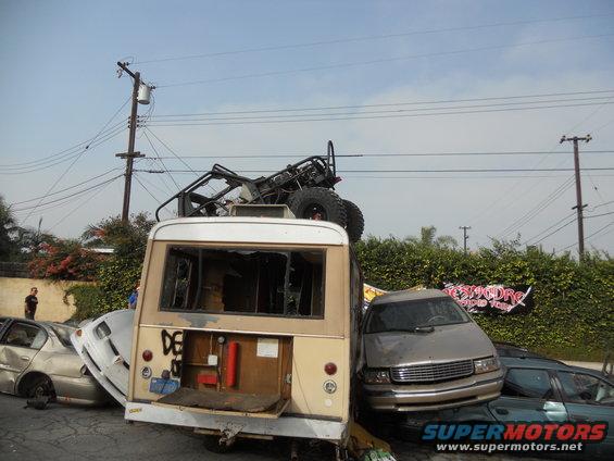 Scene of wrecked vehicles: bus, sedan, and buggy on top of bus
