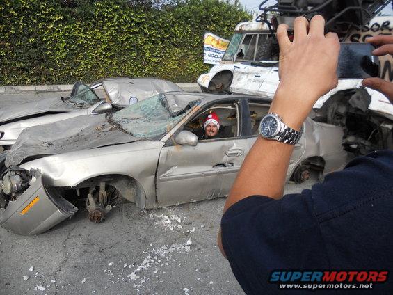 guy in santa hat in wrecked sedan, another wrecked car behind it, someone taking photo