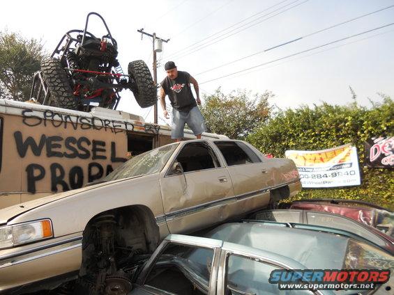 Beige sedan stacked on cars, with a buggy on a truck behind