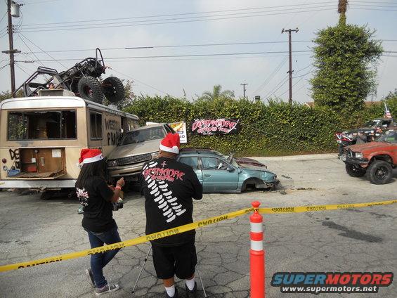 Several wrecked vehicles, including a bus with a buggy on top, and two people in Santa hats