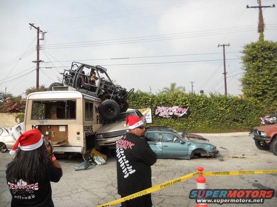 wrecked bus with a buggy on top, a sedan with its wheels missing, and an orange truck