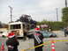 1986 Ford Bronco - A chaotic scene with multiple vehicles crushed and stacked, including a bus and a car, under a roll cage vehicle, with onlookers in festive…