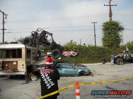 Buggy on top of a bus, with a crushed car nearby. People watching, caution tape up