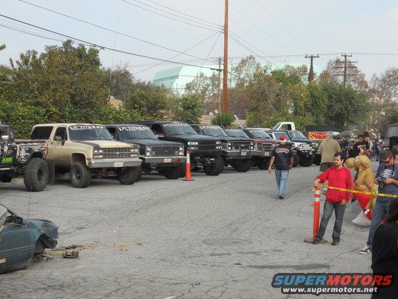 Tan and black lifted SUV parked in a line with other trucks, front view