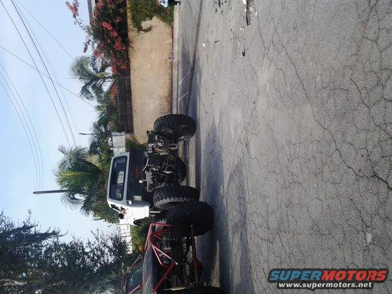 Modified off-road vehicle with large tires and roll cage, parked next to another vehicle