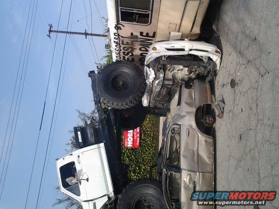 Multiple wrecked vehicles, including a silver sedan and a white car, are piled up next to a large truck with graffiti on its side