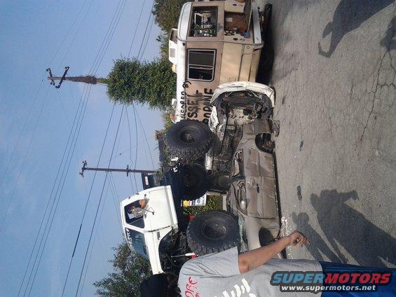 Wrecked pickup truck on its side next to an RV. Text on RV reads 'SACRED RODEO'