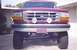 1992 Ford Bronco - This lifted Ford truck features a prominent grille and auxiliary lights, with a distinctive flag on the license plate.