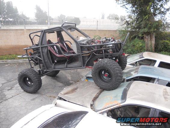Custom buggy with roll cage and racing seats sits atop a pile of wrecked cars