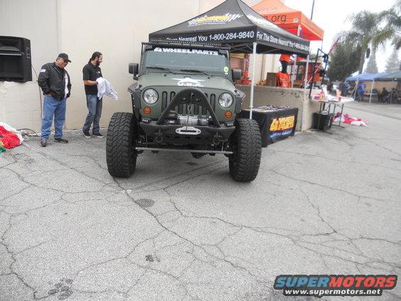 Green Jeep Wrangler JK with aftermarket bumper and winch, parked outside a tent