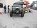 1986 Ford Bronco - A modified Jeep Wrangler JK is displayed at an outdoor event with tents and people around.