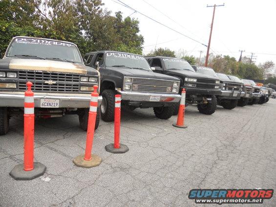 Line of lifted Chevrolet K5 Blazers and pickup trucks parked, some with 'DESMADRE' decals on windshields