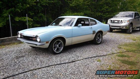 Light blue and cream 1973 Ford Maverick parked on gravel, with a silver pickup truck behind it