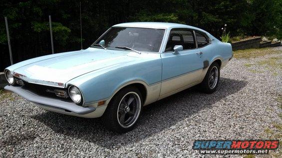 Light blue and cream 1973 Ford Maverick coupe with aftermarket wheels, parked on a gravel driveway