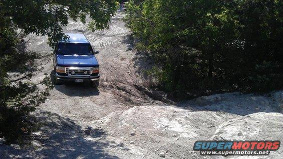 Blue SUV driving on a rough dirt road with trees around