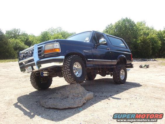 Dark blue 1995 Ford Bronco with a brush guard, driving over a rock