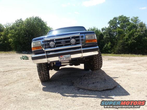 1995 Ford Bronco front view, driving over a rock on a dirt road with trees in background. License plate BY3-5006