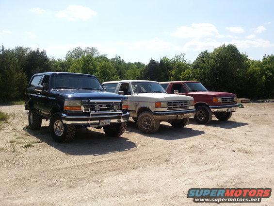 Blue 1992 Ford Bronco parked in front of a white and red SUV on a dirt lot