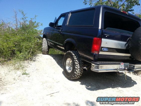 Dark blue Ford Bronco with lifted suspension and off-road tires on a dirt path