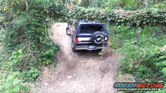 1995 Ford Bronco driving up a steep dirt trail surrounded by trees
