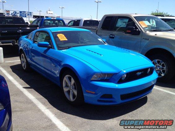 Blue 2013 Ford Mustang parked in a lot with trucks behind it