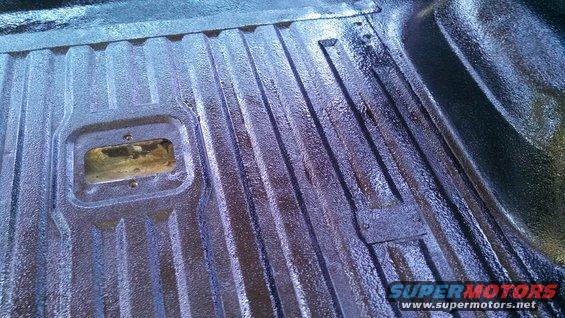 Truck bed liner with ribbed texture and a rectangular cutout. Dark blue and black
