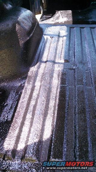 Close-up of a truck bed with a black spray-on liner, showing ribbed texture and wheel well