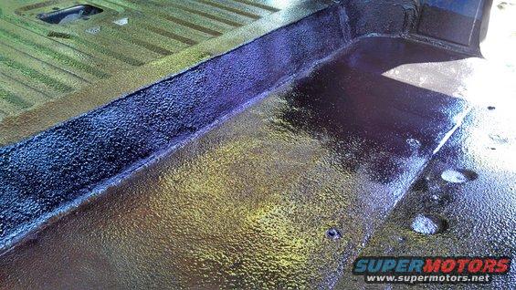 Vehicle interior floor with textured protective coating, showing a raised seam and a square cutout