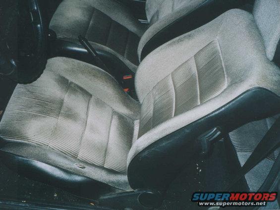 Car interior showing front seats with striped fabric and black trim. Steering wheel visible on left