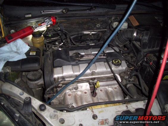 Car engine bay with tools and hoses connected to the engine