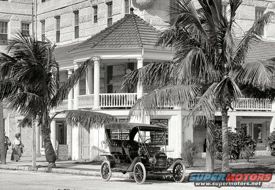 Touring car parked on street in front of building with palm trees