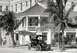 1909 Ford Model T - A vintage touring car is parked on a street in front of a building with a balcony and palm trees.