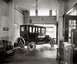 1909 Ford Model T - A dark sedan is parked inside a garage, with windows showing a reflection of a sign that reads "MOTOR CO" and "Lincoln".
