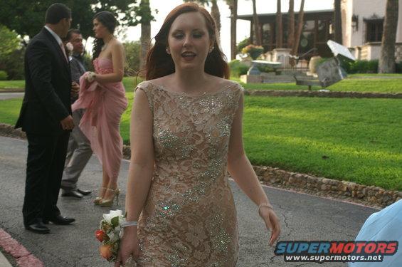 Woman in a tan dress with rhinestones, holding a corsage, walking outdoors