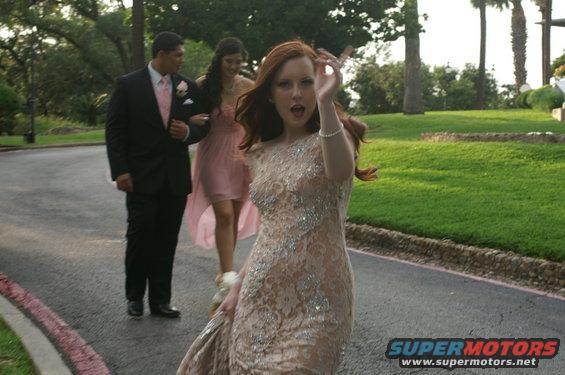 Three people in formal attire walk on a paved path next to a grassy area