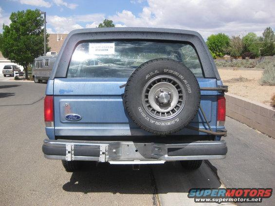 Rear view of a blue Ford Bronco with a spare tire mounted on the back. A sticker with "127-154536" is on the rear window