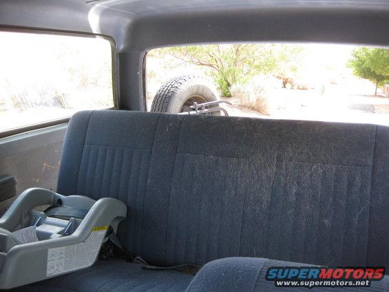 Back seat and car seat inside a vehicle, with a spare tire mounted outside the rear