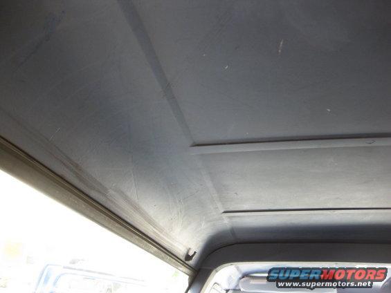 Gray vehicle interior ceiling with visible scratches and panel lines. A portion of a windshield and dashboard is visible
