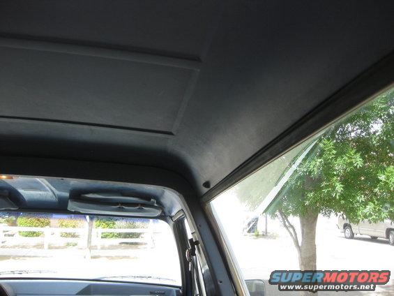 Interior view of a vehicle showing the headliner and a portion of the dashboard. Another vehicle is visible outside