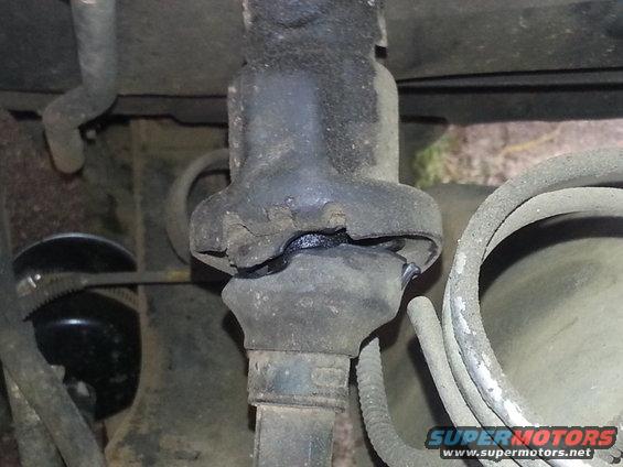 Close-up of a damaged rubber boot on a vehicle's mechanical part, showing wear and tear