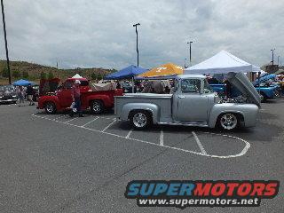 Silver 1956 Ford F-100 pickup truck and a red classic pickup truck parked at an outdoor event with tents