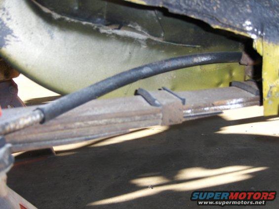 Close-up of a rusty leaf spring and black brake line under a yellow vehicle