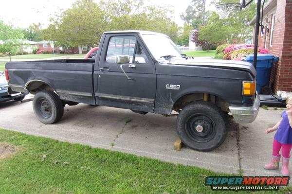 Black Ford F-250 truck, driver side view, parked on driveway with wooden blocks under wheels