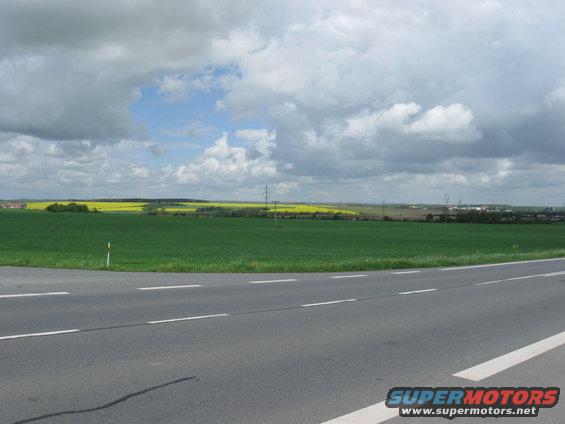 Roadway curves through green fields under a cloudy sky