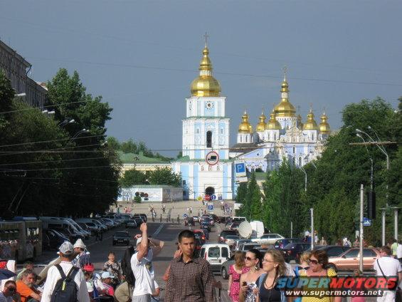 Street scene with a large blue and gold cathedral in the background and cars and people in the foreground