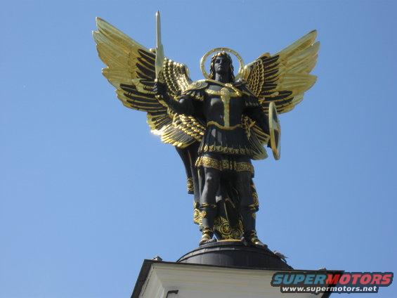 Statue of Archangel Michael with golden wings and sword against blue sky