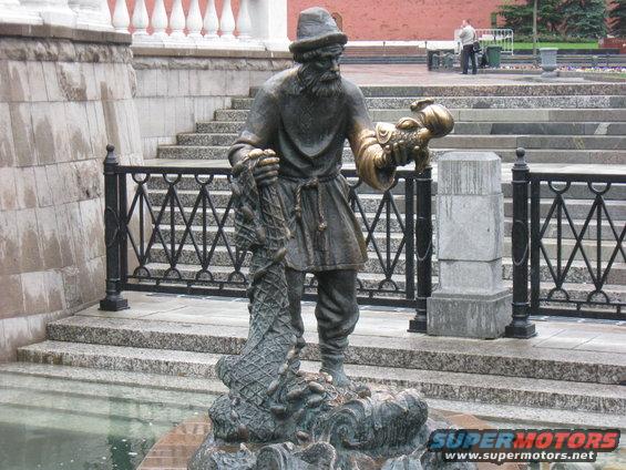 Bronze statue of a bearded man in a hat and tunic holding a fish and net, with a fountain base