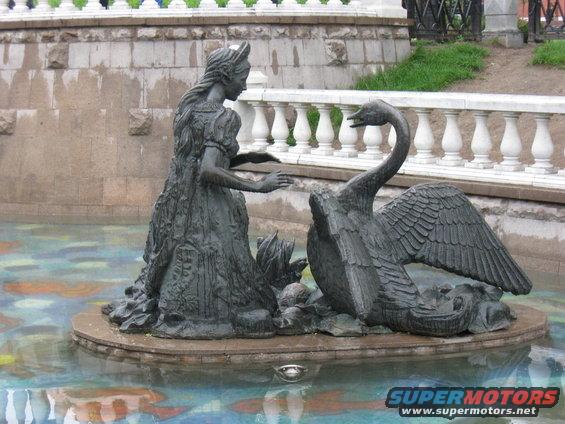 Bronze statue of a woman in a dress reaching towards a swan in a fountain