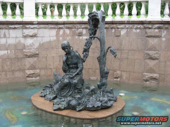 Bronze sculpture of a seated woman and a tree in a fountain with fish visible below the water